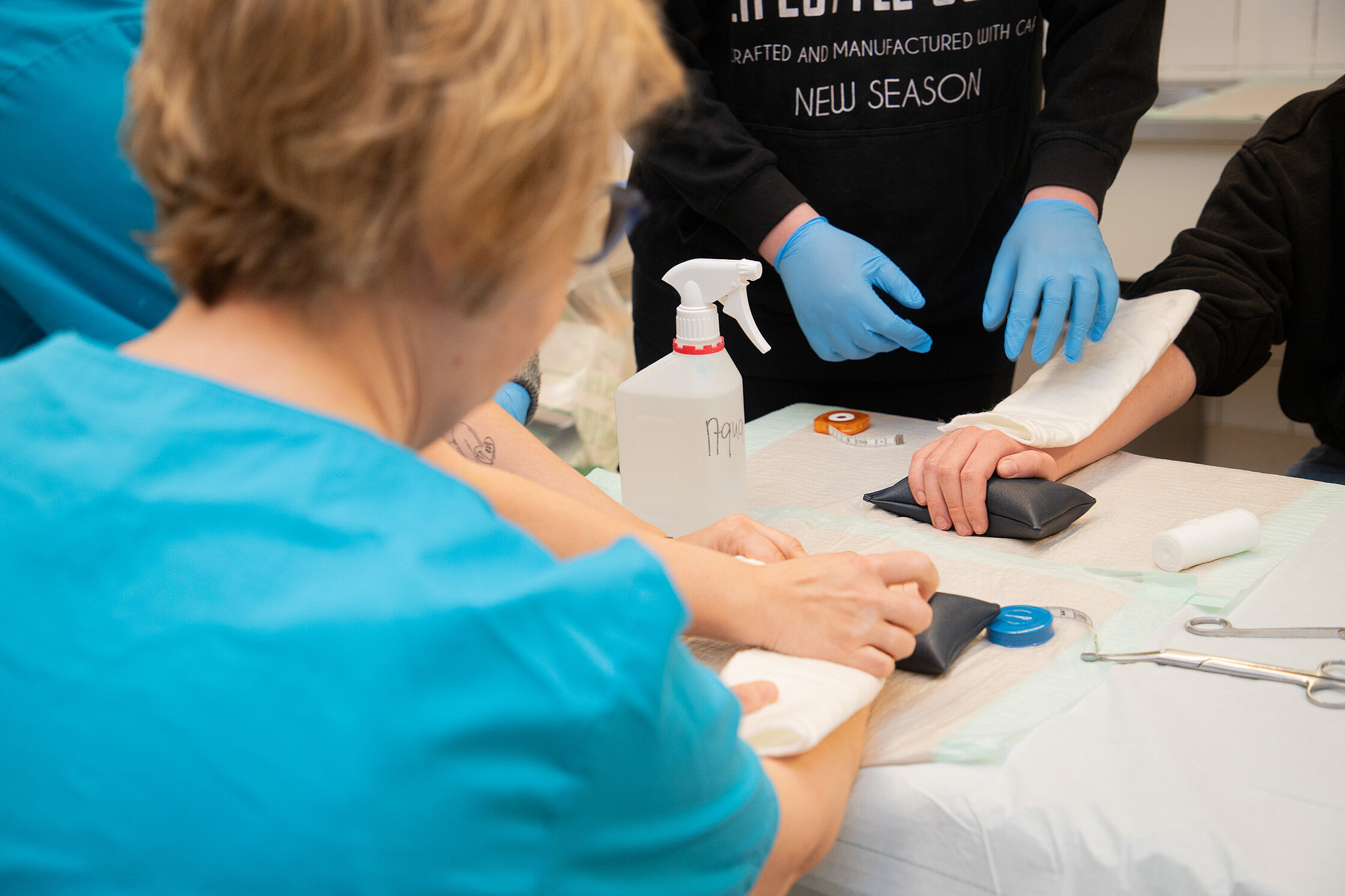 Jugendliche üben unter Anleitung das Anlegen eines Verbandes am Arm.