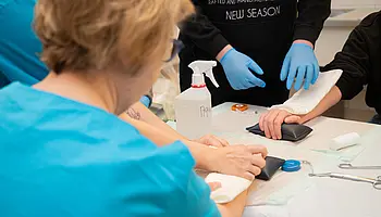 Jugendliche üben unter Anleitung das Anlegen eines Verbandes am Arm.