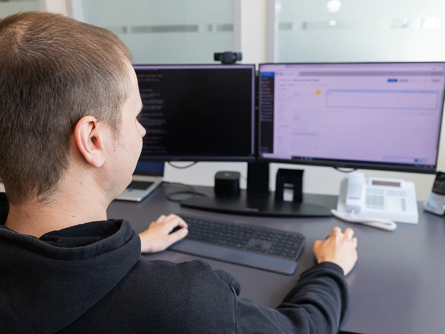 IT-Mitarbeiter arbeitet an einem Schreibtisch mit zwei Monitoren, auf denen Softwareanwendungen geöffnet sind.
