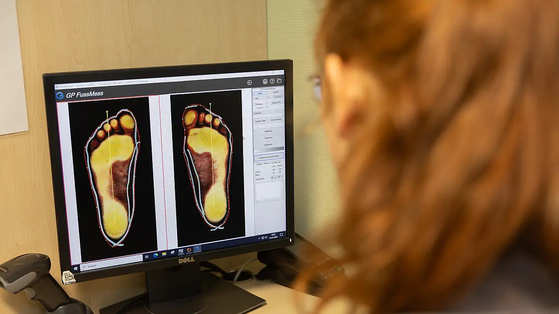 Mitarbeiterin schaut auf einen Monitor mit farbigen Darstellungen von Fußsohlen zur Belastungsanalyse.
