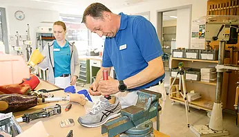 Ein Mitarbeiter zeigt einer Schülerin handwerkliche Tätigkeiten in einer Werkstattumgebung.