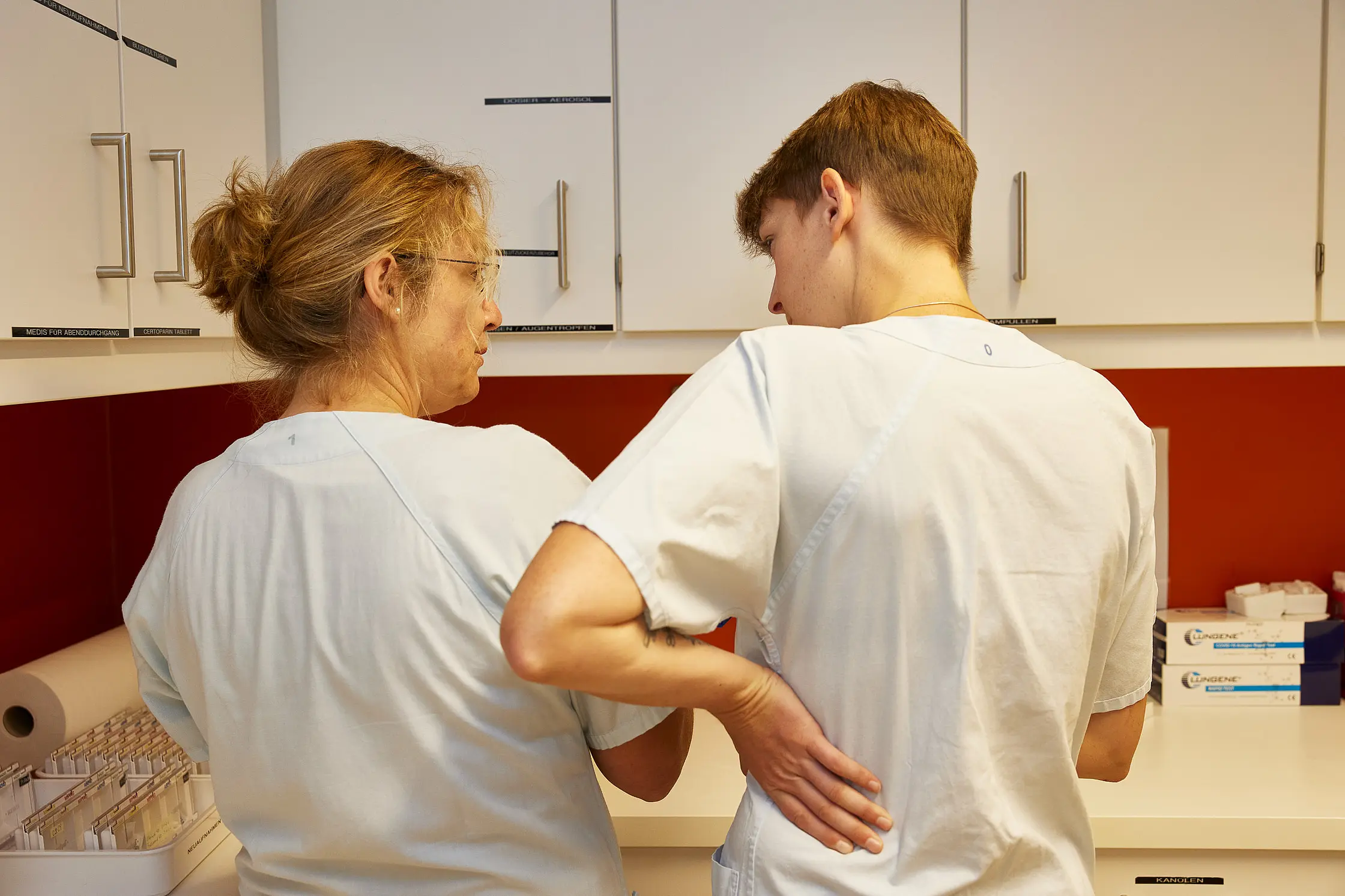 Zwei Pflegende stehen in einem Vorbereitungsraum auf Station zusammen und besprechen etwas.