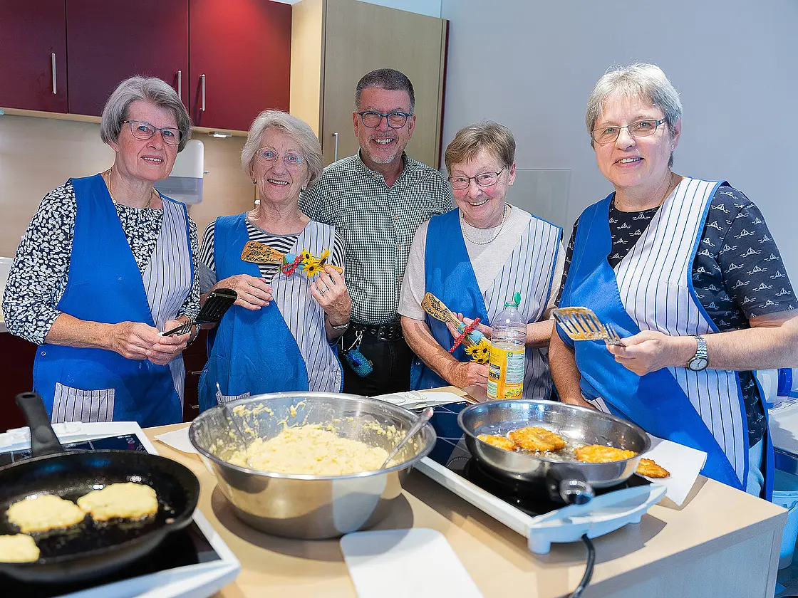 Mehrere Ehrenamtliche stehen in einer Küche und braten Reibeplätzchen in Pfannen.