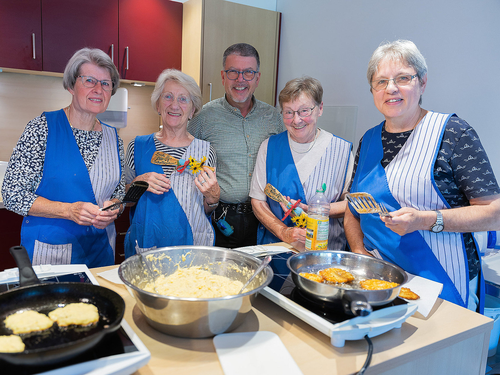 Mehrere Ehrenamtliche stehen in einer Küche und braten Reibeplätzchen in Pfannen.