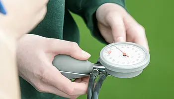 Jugendliche halten ein Blutdruckmessgerät in der Hand und lesen die Anzeige ab.