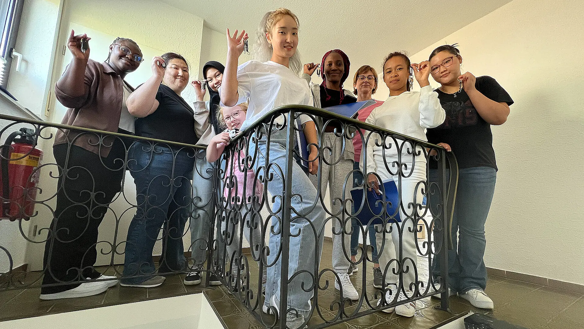 Gruppe junger Erwachsener in einem Treppenhaus, die Wohnungsschlüssel in der Hand halten.