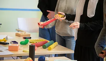 Jugendliche stehen an einem Tisch mit verschiedenen Therapie- und Trainingsmaterialien.