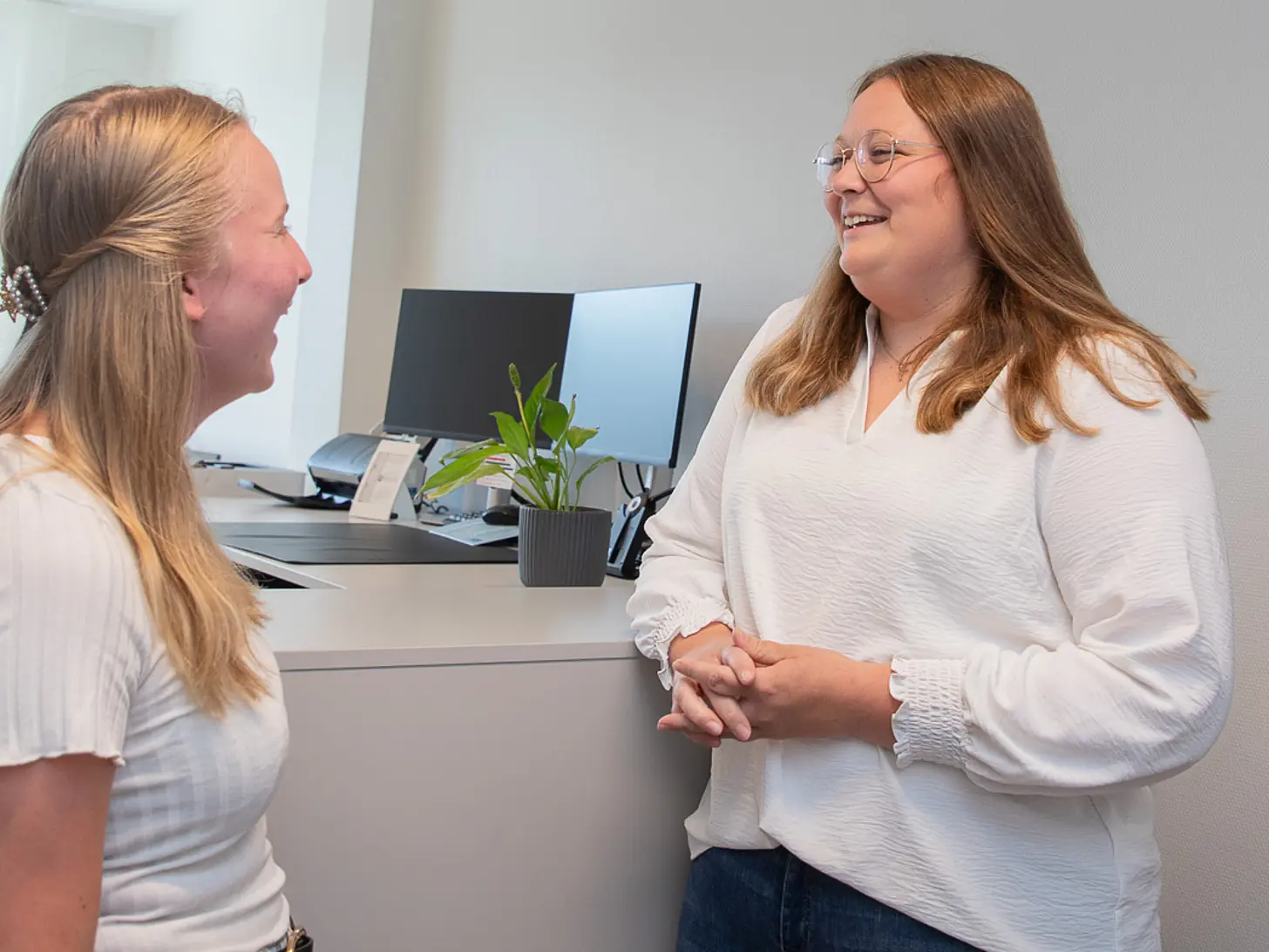 Zwei Mitarbeiterinnen stehen im Bürobereich am Empfangstresen und führen ein freundliches Gespräch.