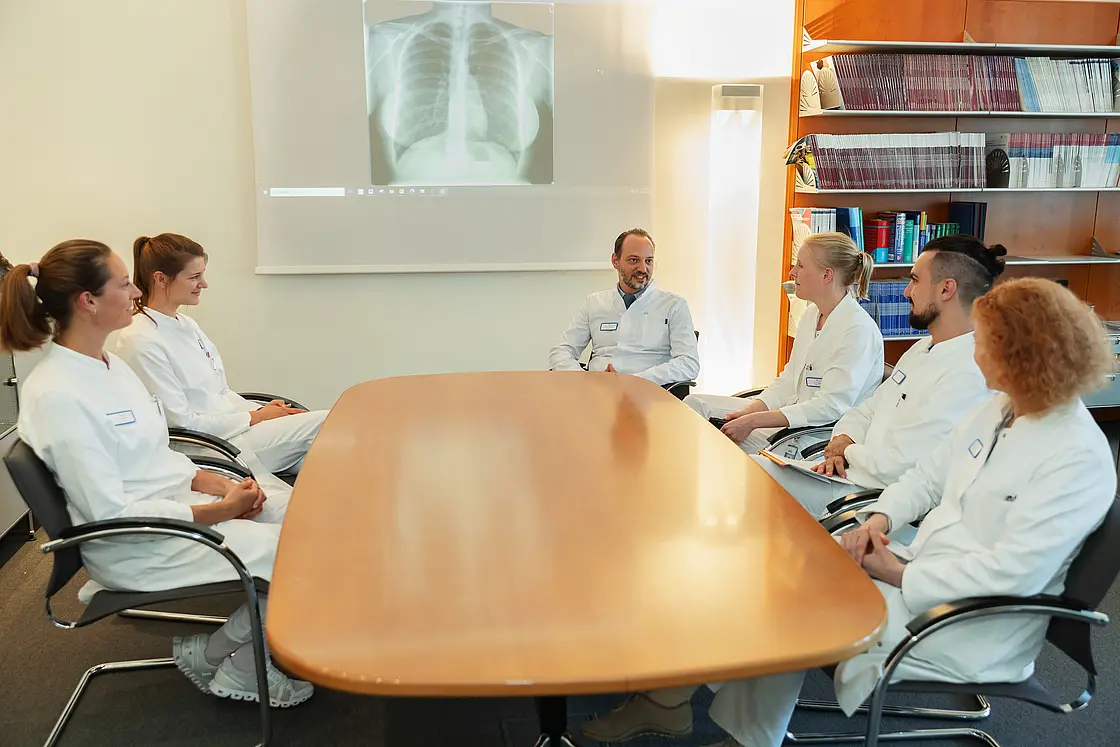 Mehrere Ärztinnen und Ärzte sitzen an einem Konferenztisch und führen eine Besprechung, PD Dr. med. Peter Korsten sitzt am Kopfende.