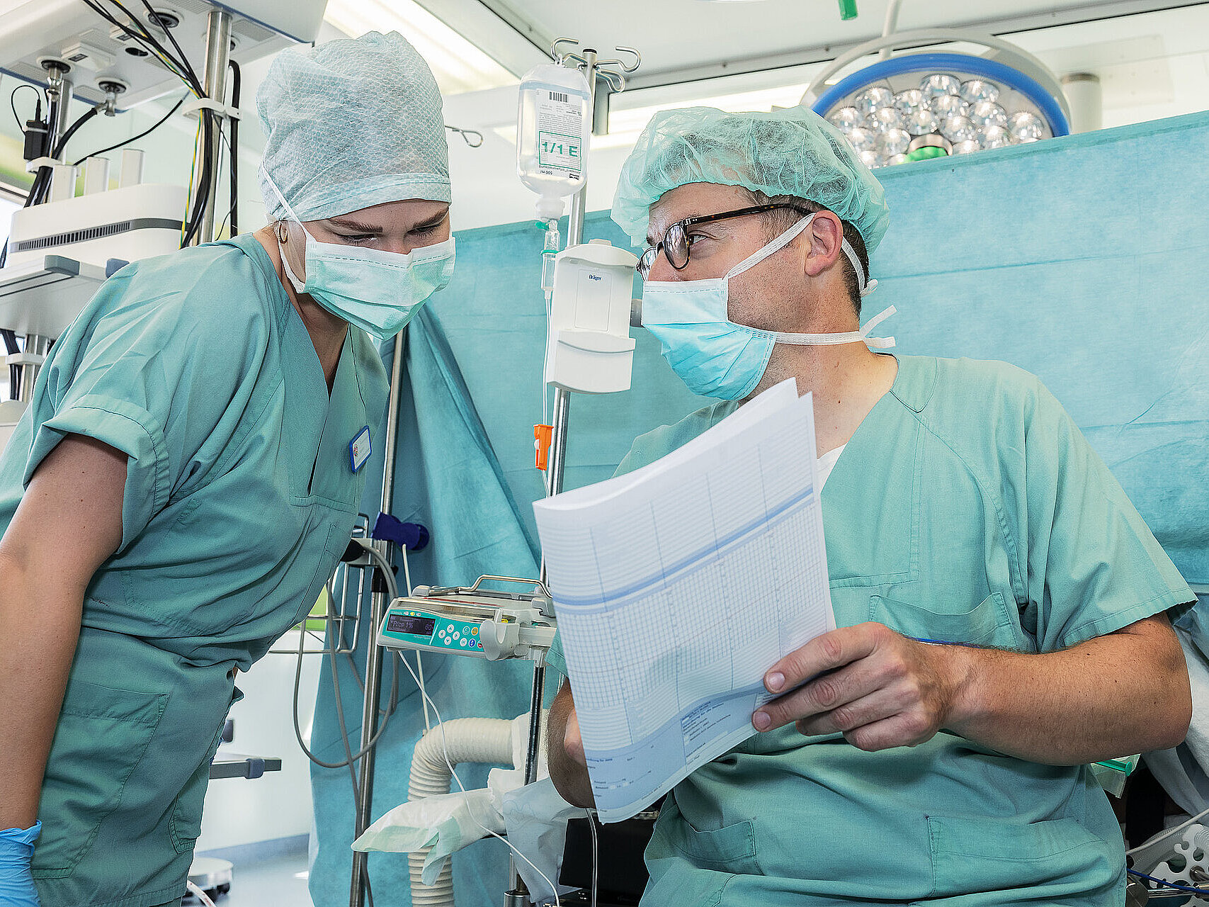 Zwei Mitarbeitende in OP-Kleidung besprechen einen Arbeitsplan direkt am Anästhesiearbeitsplatz.