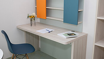 Arbeitsplatz mit Regal, Schreibtisch und dekorativer Blumenvase im Apartment.