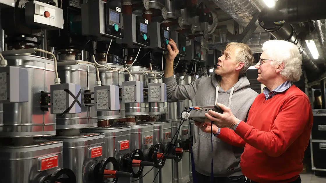 Zwei technische Mitarbeiter prüfen Steuerungs- und Pumpentechnik in einem Technikraum des St. Josef-Stifts.