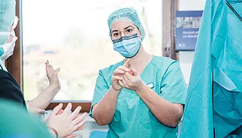 Mitarbeitende im OP-Bereich erklären Jugendlichen Schutzkleidung und hygienisches Arbeiten.