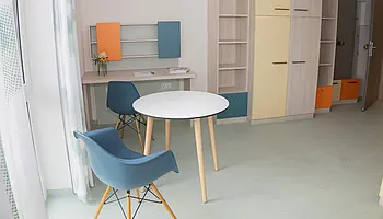 Apartmentzimmer mit rundem Tisch, zwei Stühlen, Schreibtisch und Kleiderschrank.