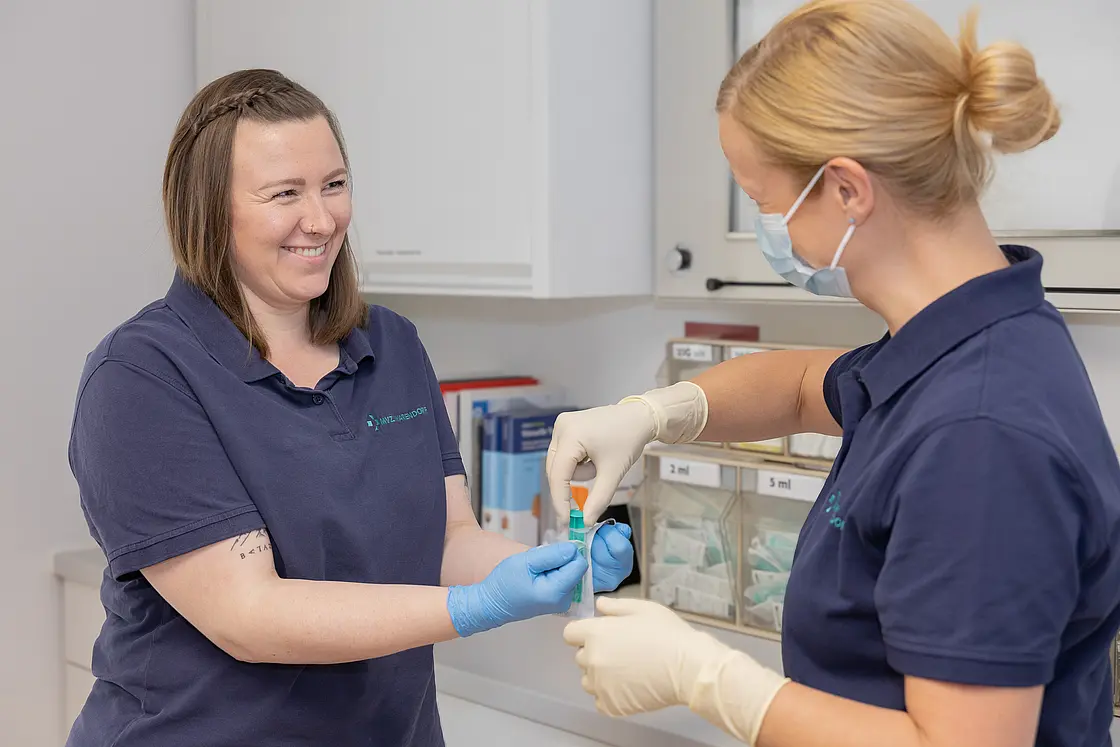 Zwei Mitarbeiterinnen des MVZ Warendorf bereiten im Praxisraum gemeinsam eine Blutprobe vor; eine trägt Handschuhe und hält ein Probenröhrchen.