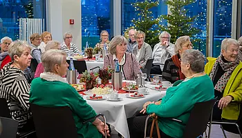 Gruppe von ehrenamtlich Engagierten sitzt an festlich gedeckten Tischen bei einer gemeinsamen Veranstaltung im Klinikgebäude.