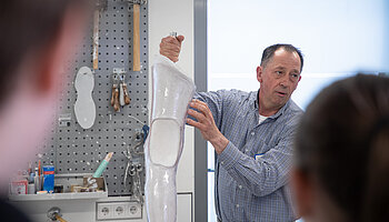 Ein Mitarbeiter erklärt einer Gruppe ein Prothesenmodell in einer Werkstatt.