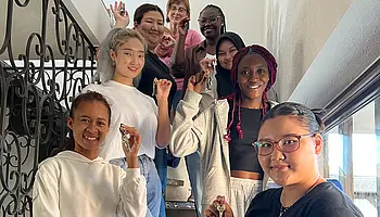 Gruppe junger Erwachsener in einem Treppenhaus, die Wohnungsschlüssel in der Hand halten.