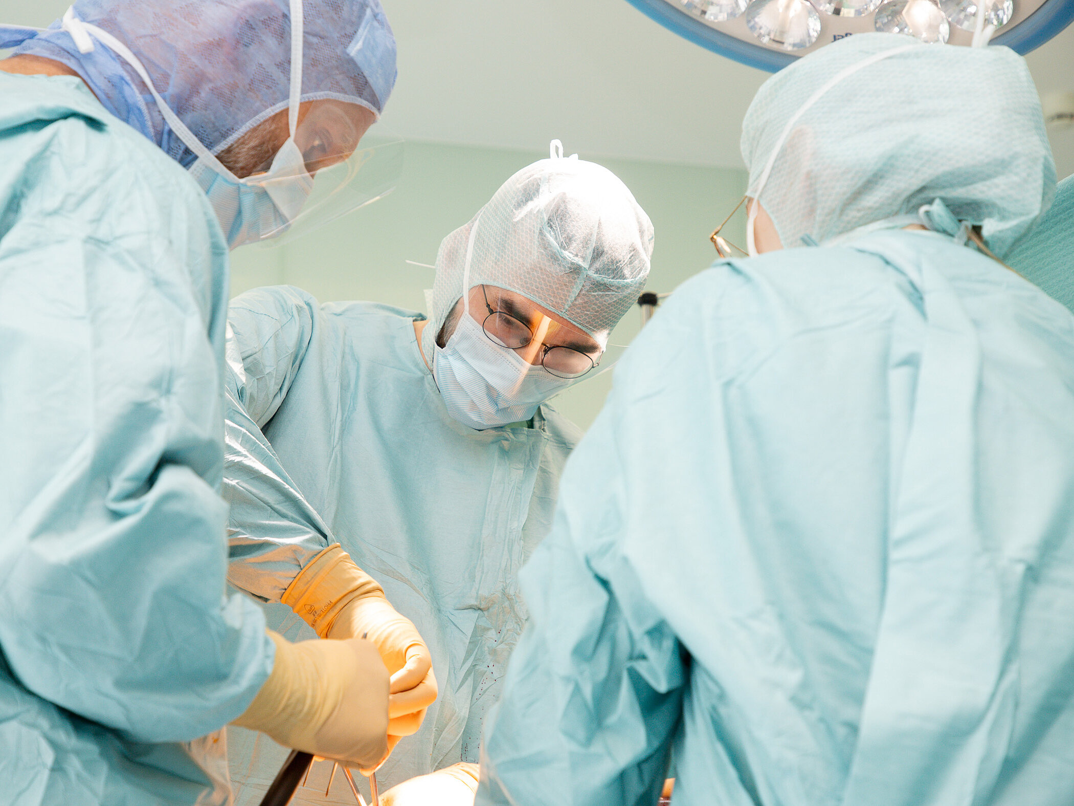 Mehrere Personen in OP-Kleidung stehen dicht um einen Operationstisch und arbeiten gemeinsam an einem Eingriff.