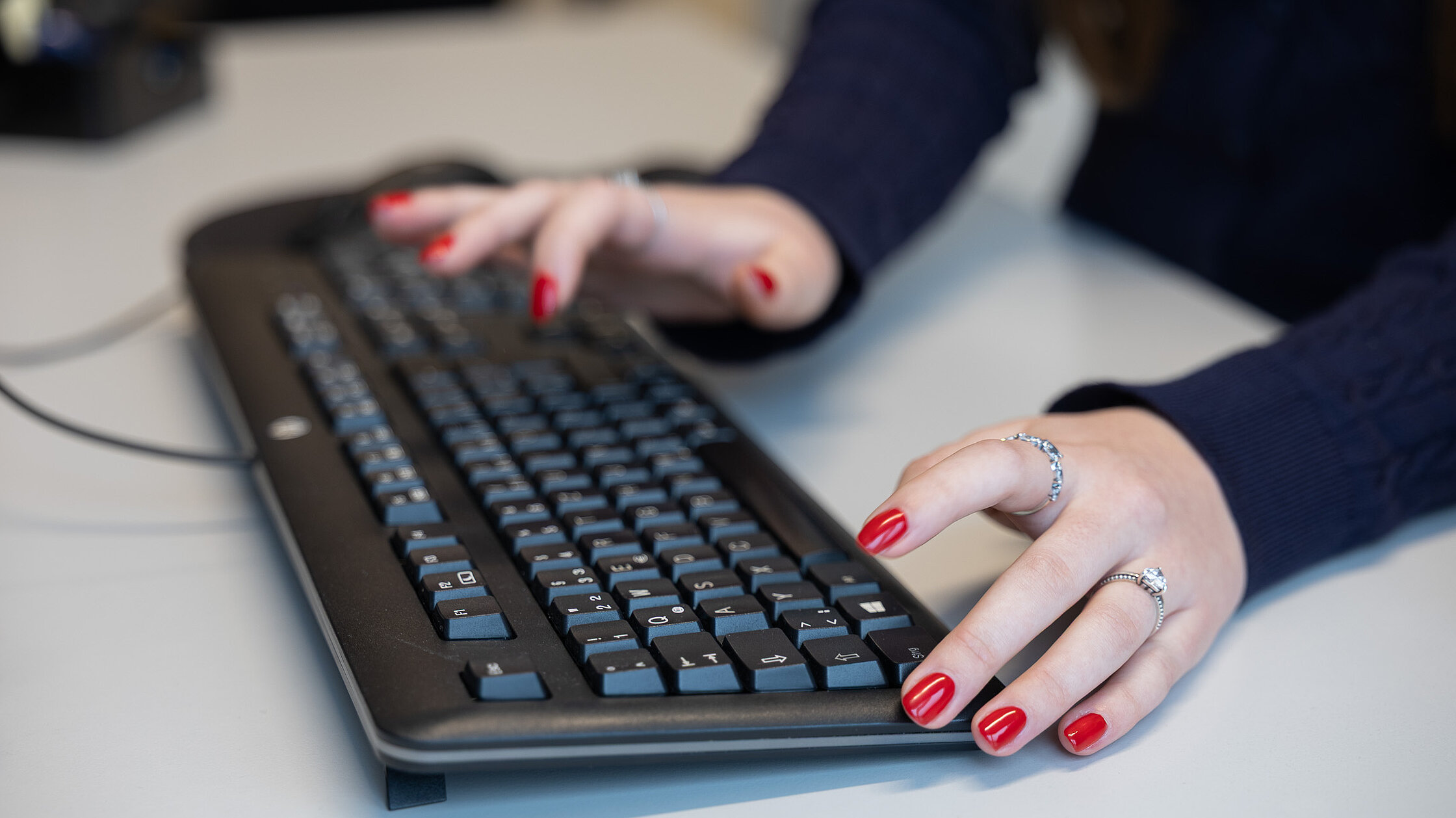 Zwei Hände tippen auf einer Computertastatur an einem Schreibtisch.