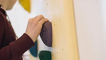 Eine Person greift an einer Therapiewand nach bunten Klettergriffen.