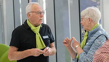 Zwei ehrenamtlich Engagierte unterhalten sich im Klinikflur und tragen das grüne Erkennungszeichen der Krankenhaushilfe.