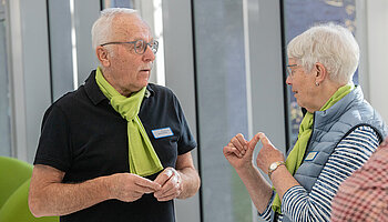 Zwei ehrenamtlich Engagierte unterhalten sich im Klinikflur und tragen das grüne Erkennungszeichen der Krankenhaushilfe.