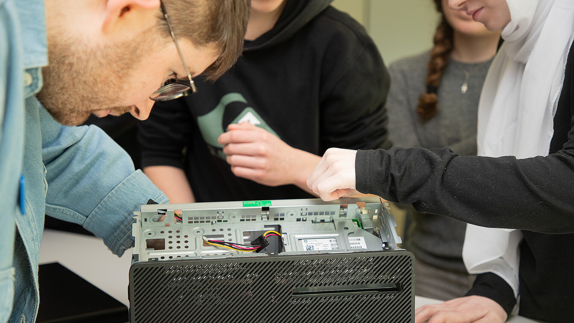 Jugendliche öffnen gemeinsam mit einem Mitarbeitenden das Gehäuse eines Computers.
