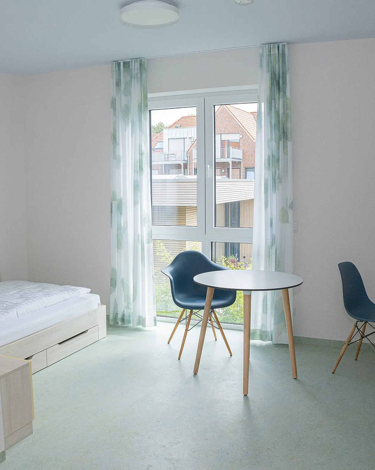 Modern eingerichtetes Apartment mit Bett, Schreibtisch, Stuhl und kleinem Tisch am Fenster.