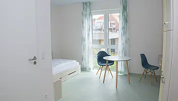 Schreibtisch mit Stuhl und Regal in einem hellen Apartmentraum.