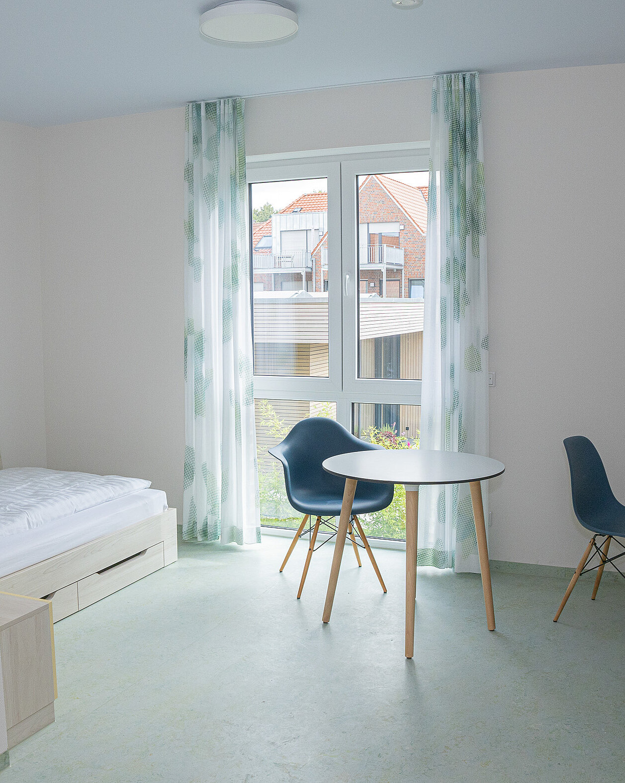 Modern eingerichtetes Apartment mit Bett, Schreibtisch, Stuhl und kleinem Tisch am Fenster.