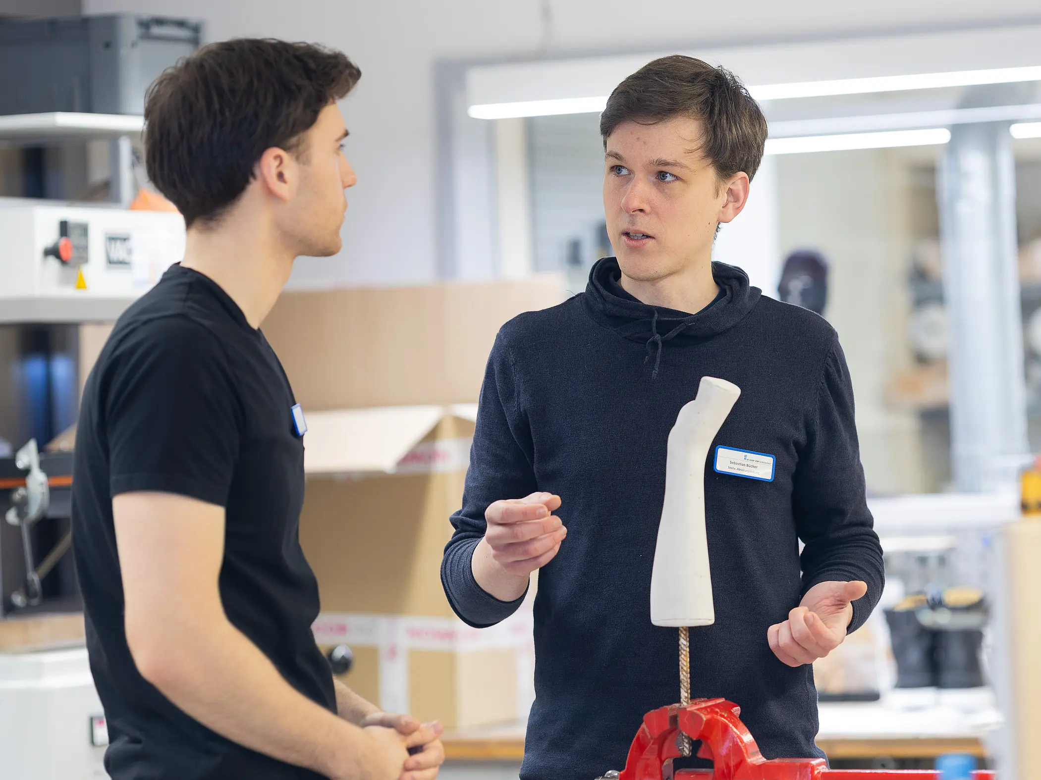 Zwei Mitarbeiter stehen an einem Arbeitsplatz und besprechen ein Gipsleistenmodell, das in einem Schraubstock fixiert ist.