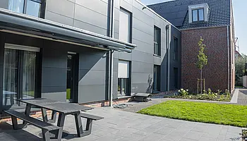 Außenbereich des Apartmenthauses mit Terrasse, Sitzbank und gepflegter Rasenfläche.