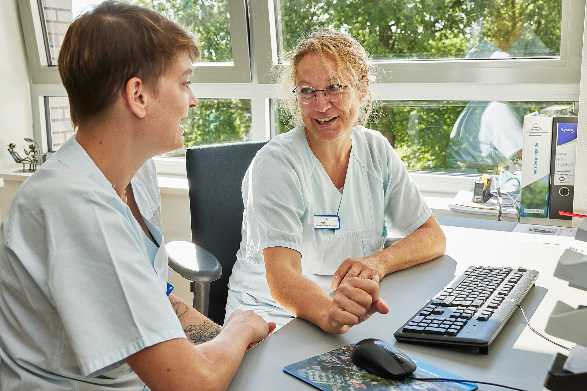 Ausbildung in der Pflege: Zwei Pflegekräfte sitzen an einem Schreibtisch und sprechen über Inhalte auf einem Computerbildschirm.